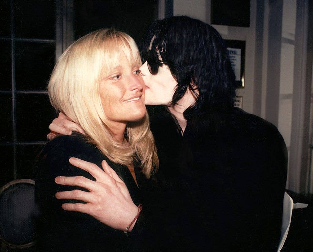 Michael Jackson holds Debbie Rowe's shoulder and the back of her neck, kissing her cheek.