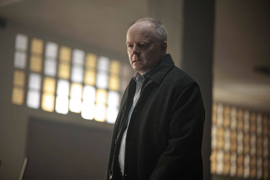 Jason Watkins stands in a prison visitor room, wearing a black jacket and light blue shirt.