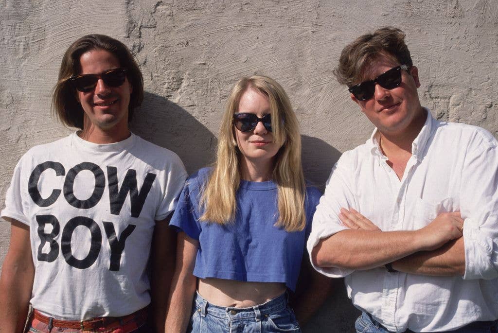 Pop group the Tom Tom Club, including Tina Weymouth (C) and Chris Frantz (R), posing in front of a wall. 