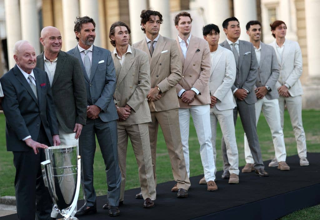 Rod Laver and Patrick Rafter stand with other men in suits, one holding a trophy.