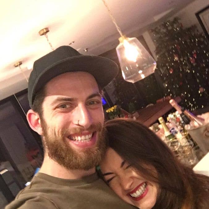 Man with beard and cap smiling with Lacey Turner, both laughing in a festive setting.
