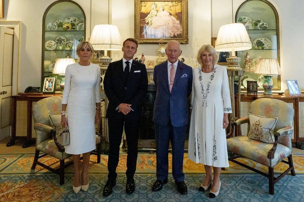 Emmanuel Macron and King Charles with their spouses in formal attire in a grand room.