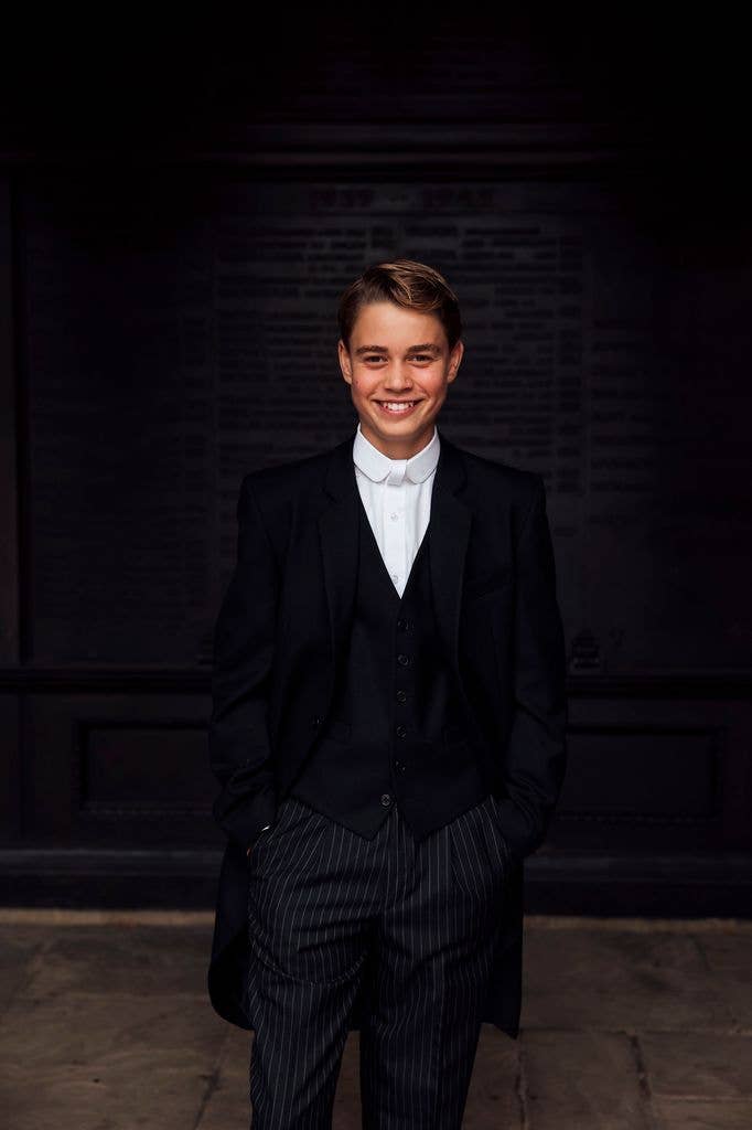 Prince George of Cambridge smiling in a black suit and white shirt.