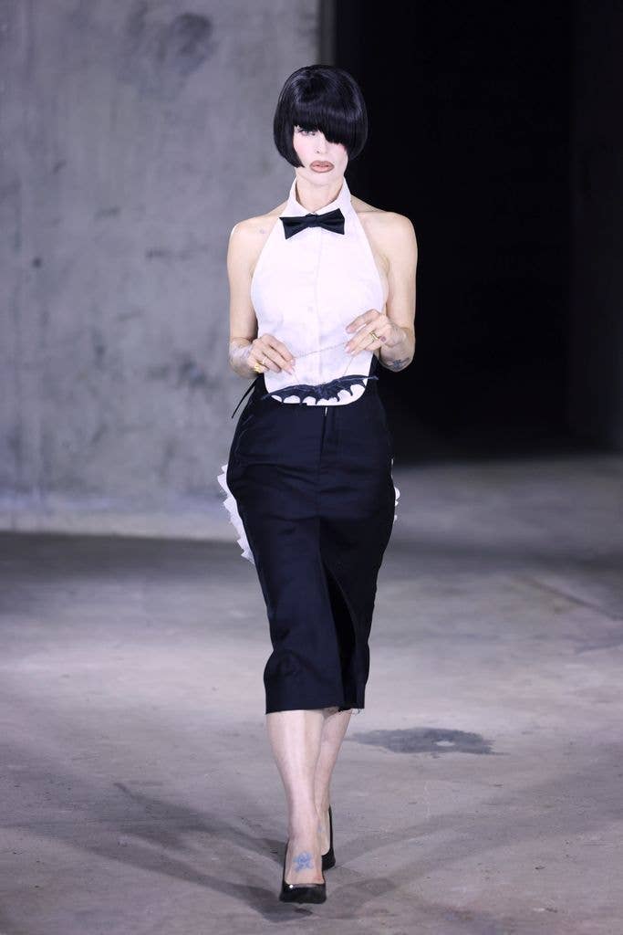 Kelly Osbourne wearing a short black wig and tuxedo shirt walking on a runway at LFW