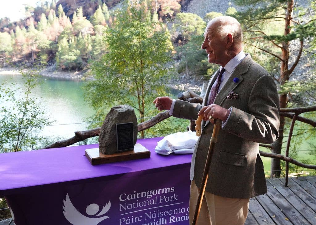 King Charles smiling next to a stone in front of a lake in scotland