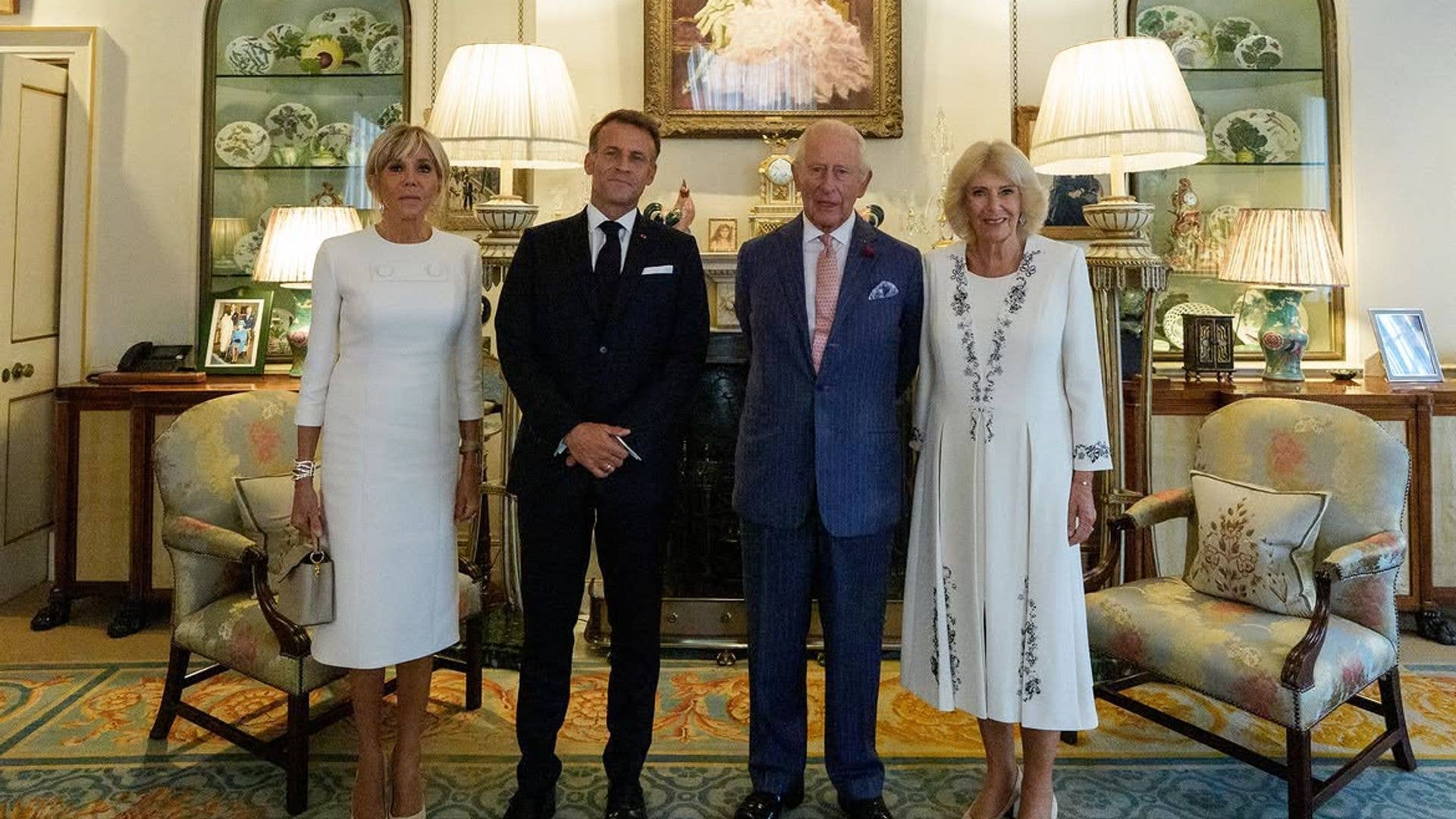Emmanuel Macron and King Charles with their spouses in formal attire in a grand room.