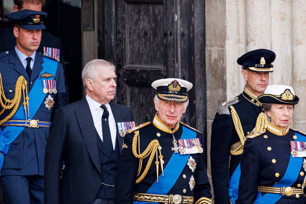 Andrew Mountbatten-Windsor in a blue suit behind King Charles