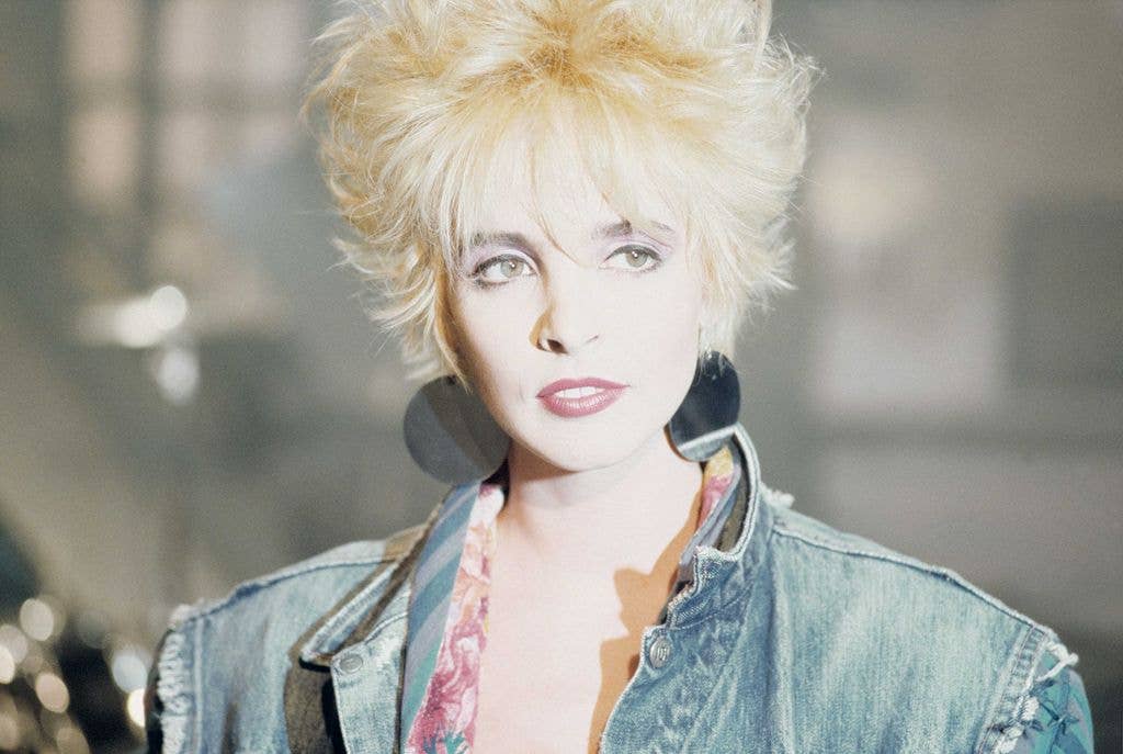 Nena, a blonde-haired woman with spiky hair, wearing a denim jacket and large hoop earrings.