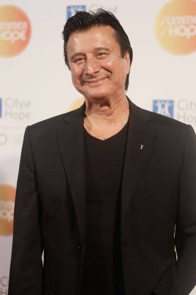 Steve Perry smiling, wearing a black suit and black shirt, at an event.