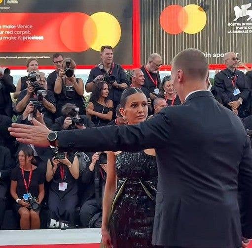 Nina Dobrev standing by a man raising his arm on Venice International Film Festival red carpet