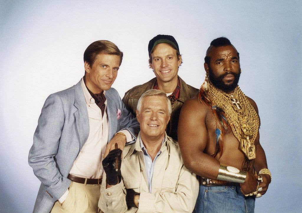 A promotional group portrait of The A-Team cast, with Dirk Benedict, George Peppard and Dwight Schultz standing together and Mr. T at the front wearing gold chains.