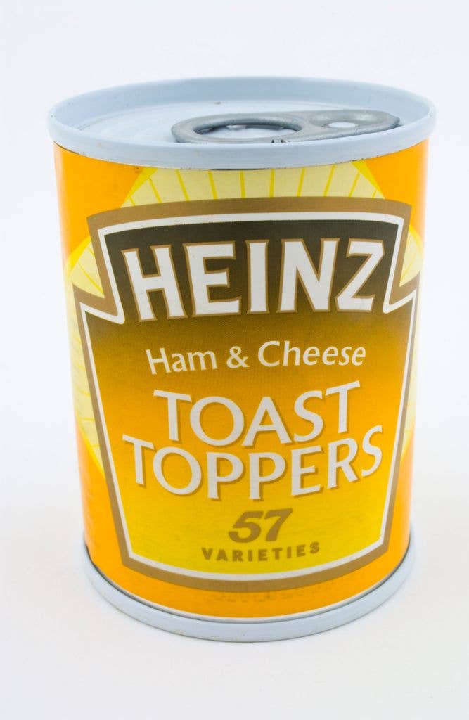 A ring-pull tin of Heinz Ham and Cheese Toast Toppers stands against a plain white background, its orange label showing the classic Heinz shield and 57 Varieties mark.