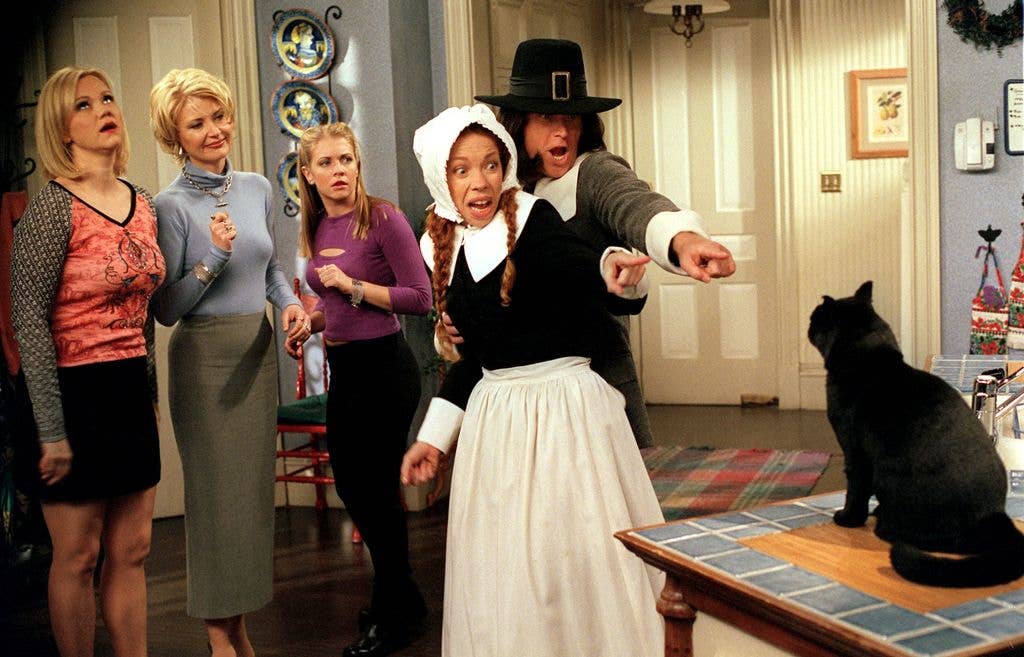 A Thanksgiving-themed scene from Sabrina, the Teenage Witch, with Caroline Rhea, Beth Broderick and Melissa Joan Hart watching as Jennifer Butt and Christopher Rich, dressed as pilgrims, point towards something off-camera, with a black cat sitting nearby.