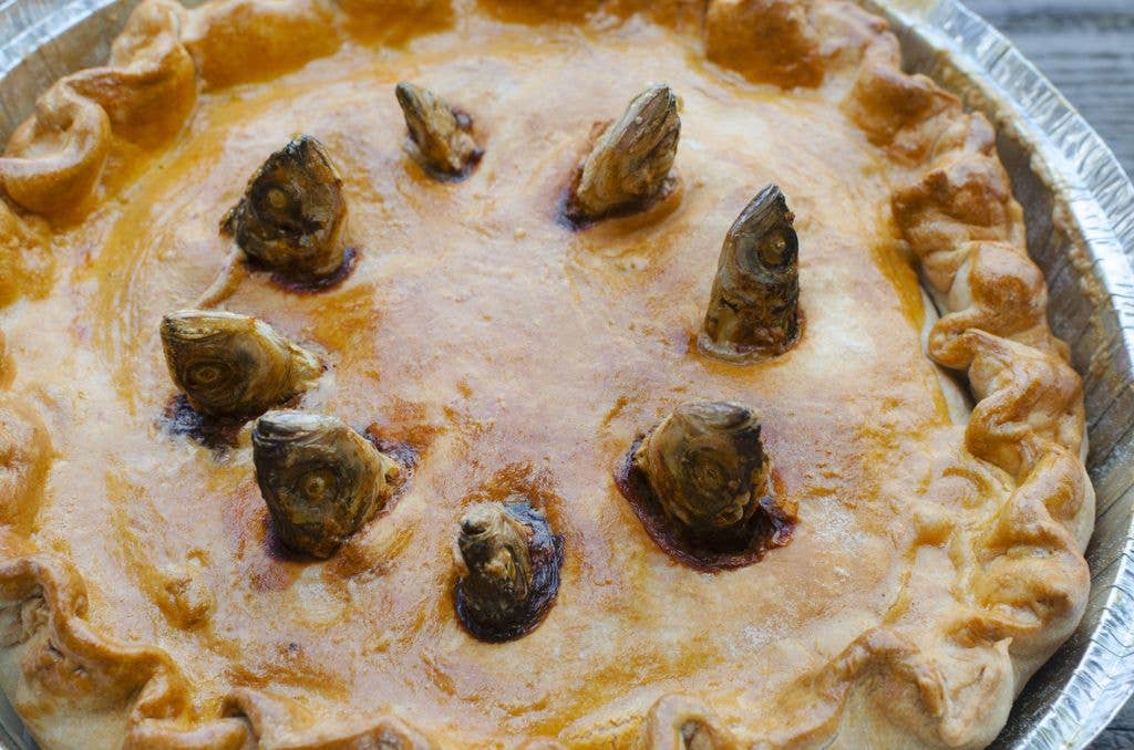 A baked pie with a crimped golden pastry crust, its surface pierced by several small fish heads arranged in a circle.