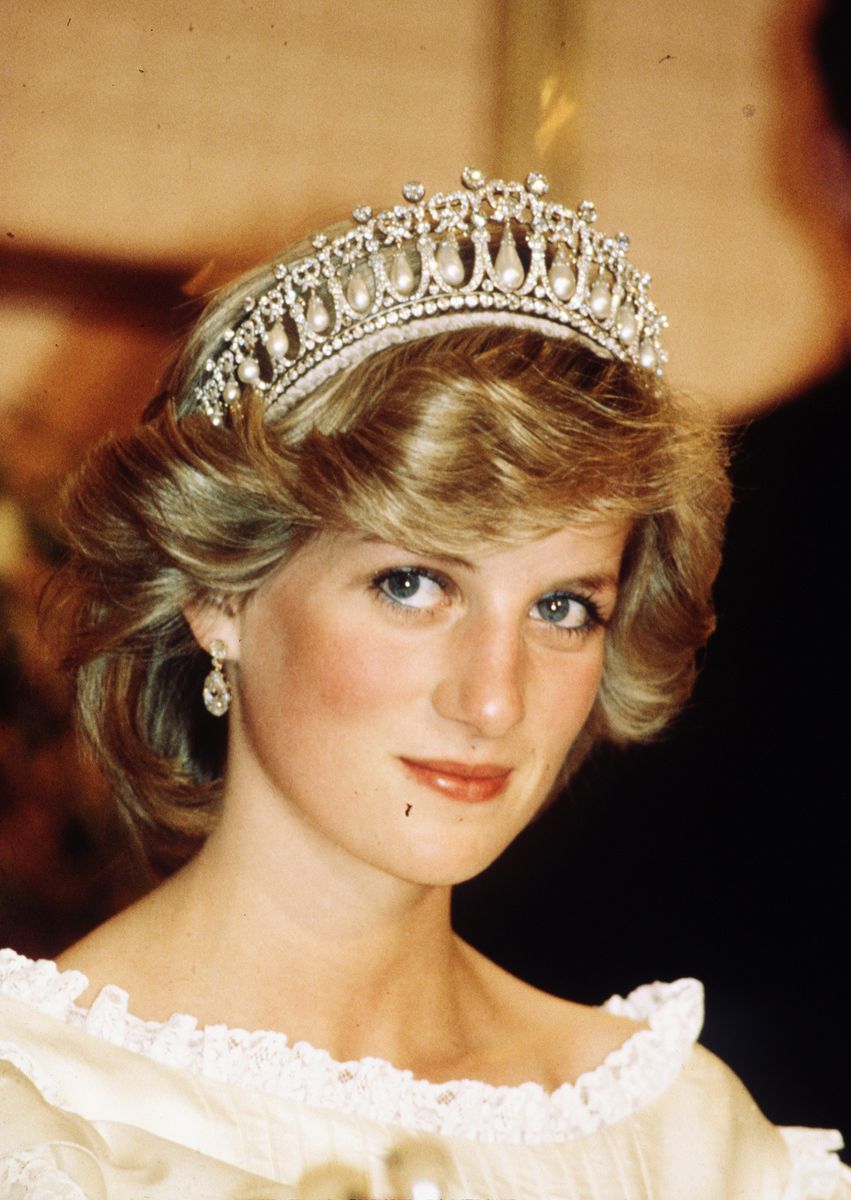 Diana, Princess of Wales, wearing a cream satin dress by Gina Fratini with the Queen Mary Cambridge Lover's Knot Tiara and diamond earrings attends a banquet on April 29, 1983 