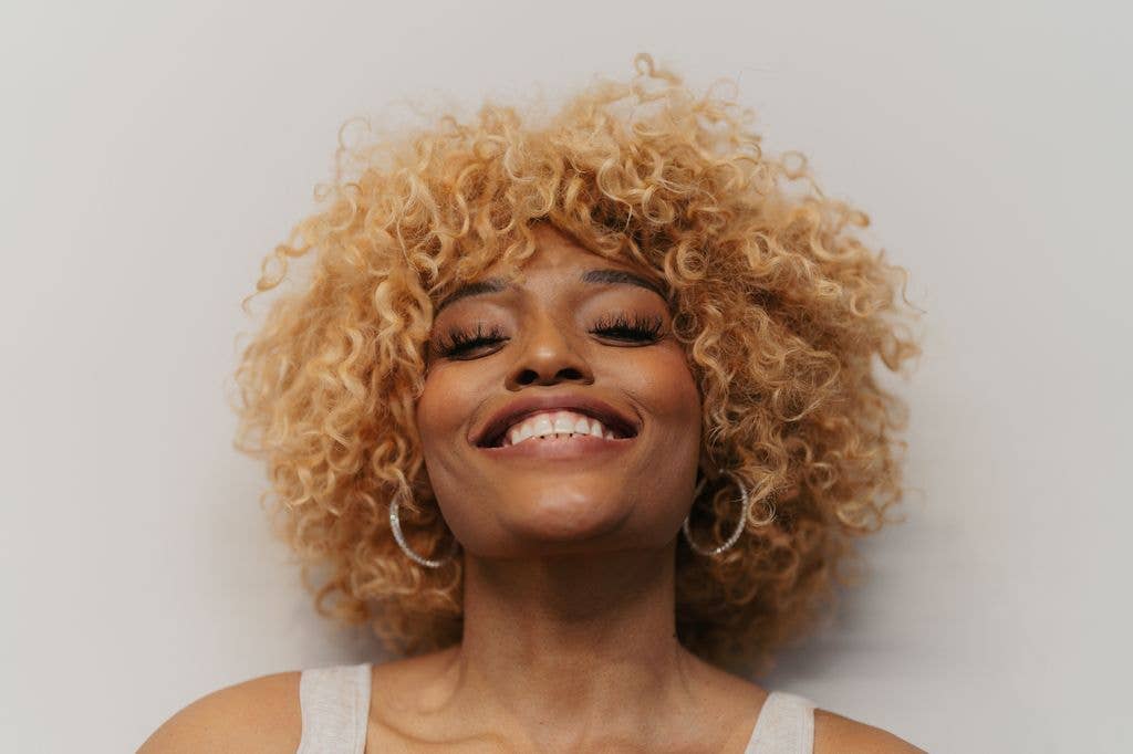 woman with curly blonde hair smiling and wearing hoop earrings and a white tank top