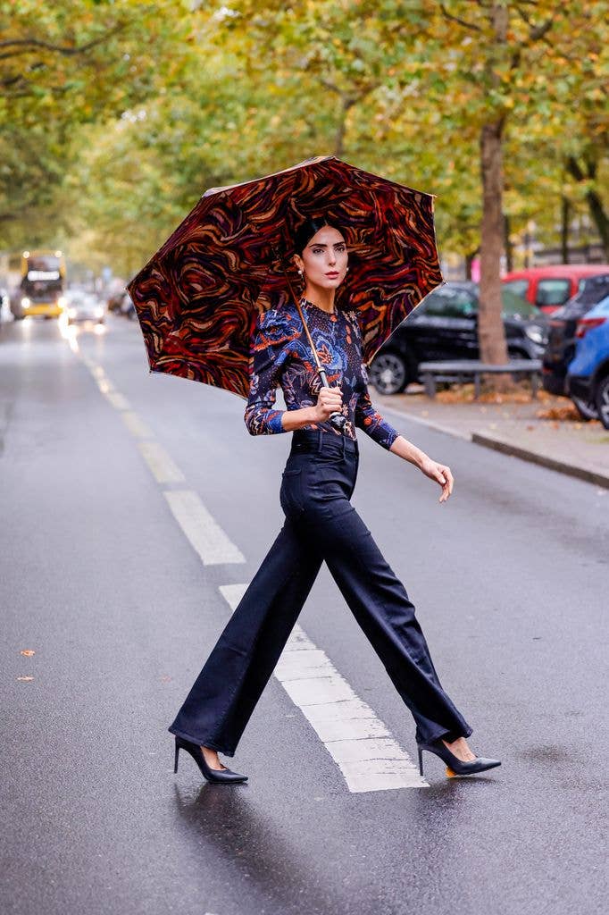 BERLIN, GERMANY - OCTOBER 19:  Model Zoe Helali, wearing black wide leg trousers by Mother, a multicolored body by Farm Rio, jewelry by Meerglanz, black pumps by Maison Baum and an umbrella by Pasotti, seen on October 19, 2025 in Berlin, Germany. (Photo by Streetstyleshooters/Getty Images)