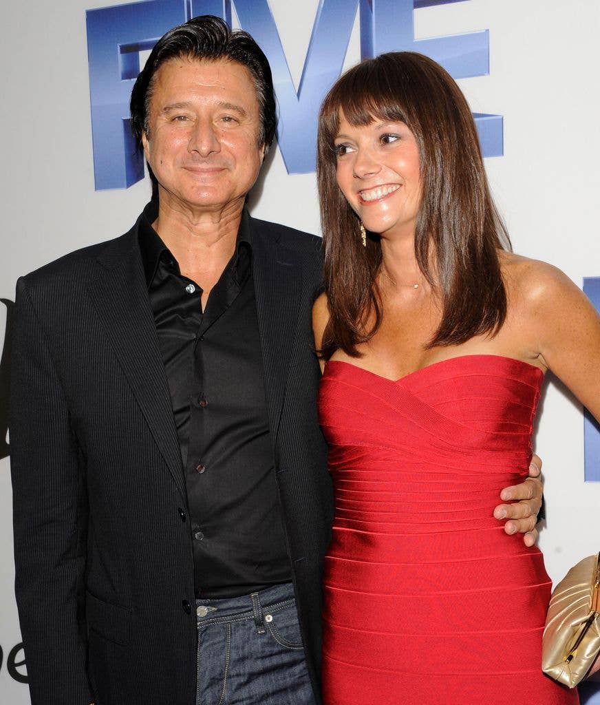 Steve Perry and a woman in a red dress pose for a photo, smiling.