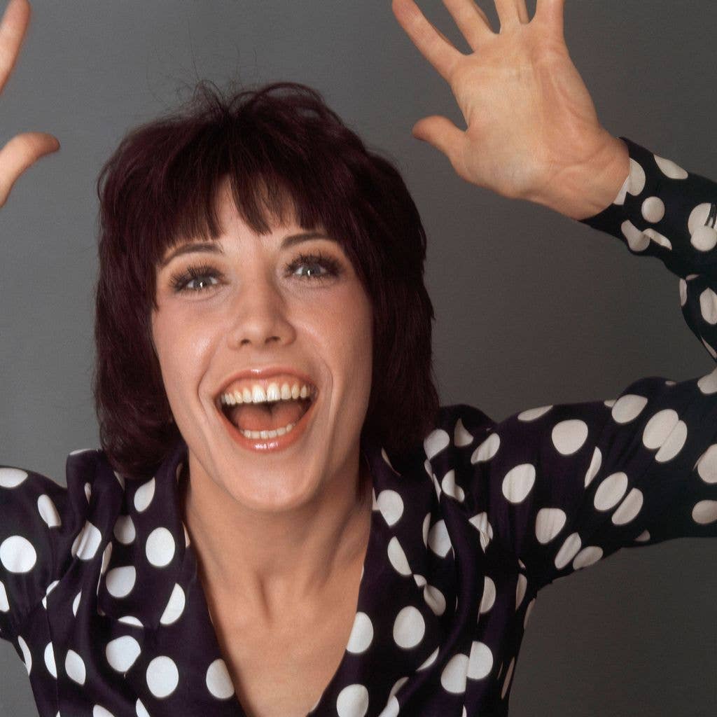 American actress and comedian Lily Tomlin wearing a black-and-white polka-a-dot print blouse; she is laughing and looking into the camera lens with both arms up  in 1971