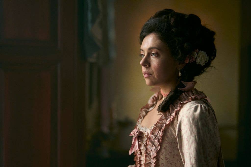 Bel Powley in a pink ruffled dress, looking off-camera with a thoughtful expression.
