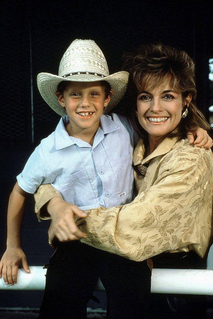 Linda Gray and Omri Katz smiling and hugging, standing by a white rail.