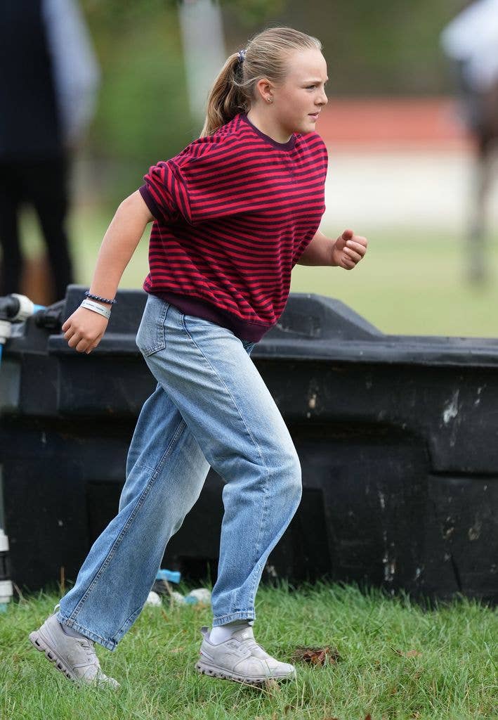 Mia Tindall, wearing a striped top and jeans, jogs across the grass at a horse trials event.