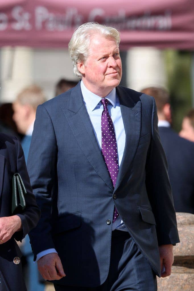 Charles Spencer, 9th Earl Spencer, in a navy suit and purple tie, walks with others under a pink canopy.