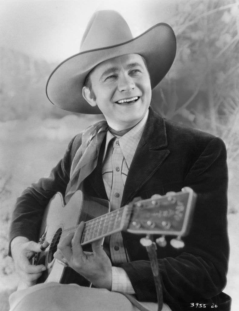 American singer and actor Tex Ritter posed in a publicity photo strolling his guitar, circa 1935.