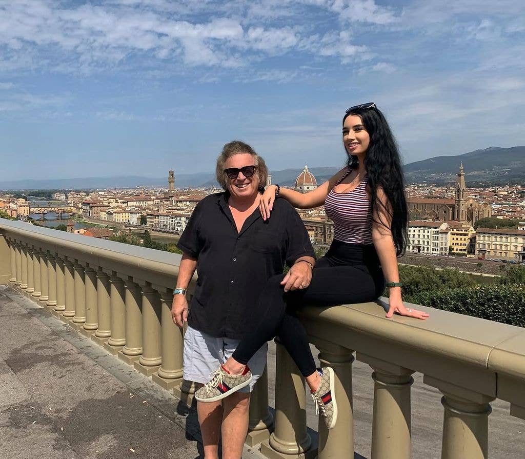 Don McLean stands smiling in sunglasses beside a young woman perched on a stone balustrade, with the city of Florence, its bridges and domed cathedral visible in the distance.