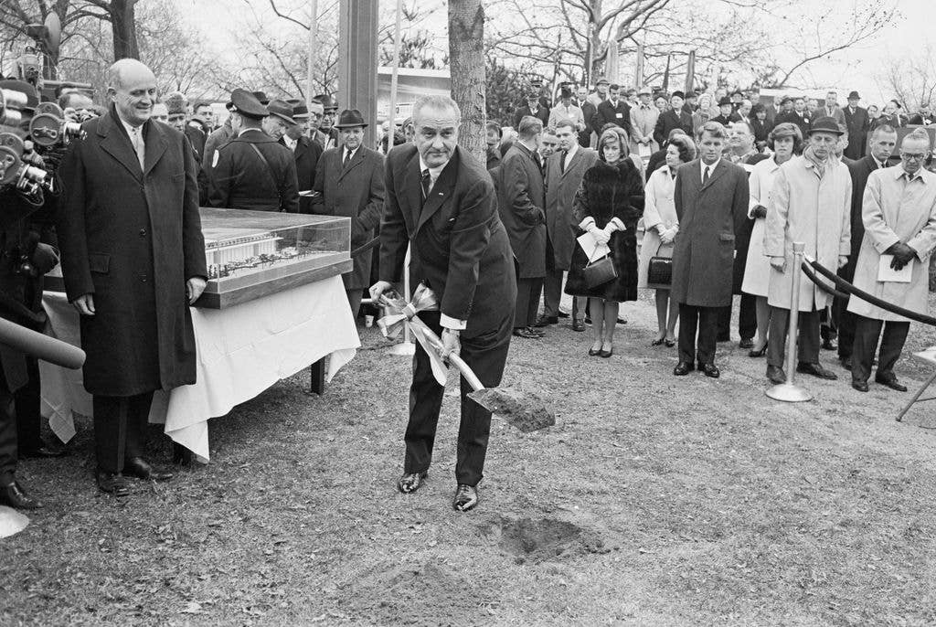 With members of the Kennedy family looking on, president Johnson lifts a shovel full of dirt during ground-breaking ceremonies for the John F. Kennedy Center for the Performing Arts. Watching are Mrs. Jean Smith, the late President's sister; Mrs. Lyndon B. Johnson; Robert F. Kennedy; and Mrs. eunice Shriver, another sister. 1964
