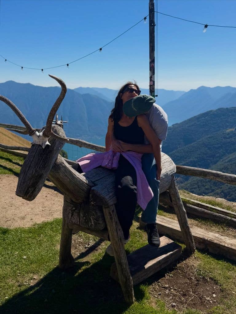 Jason kisses Katie on the neck whilst she is sitting on top of a wooden horse in the mountains