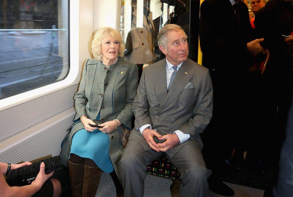 Charles, Prince of Wales, and Camilla, seated on a train, dressed formally.
