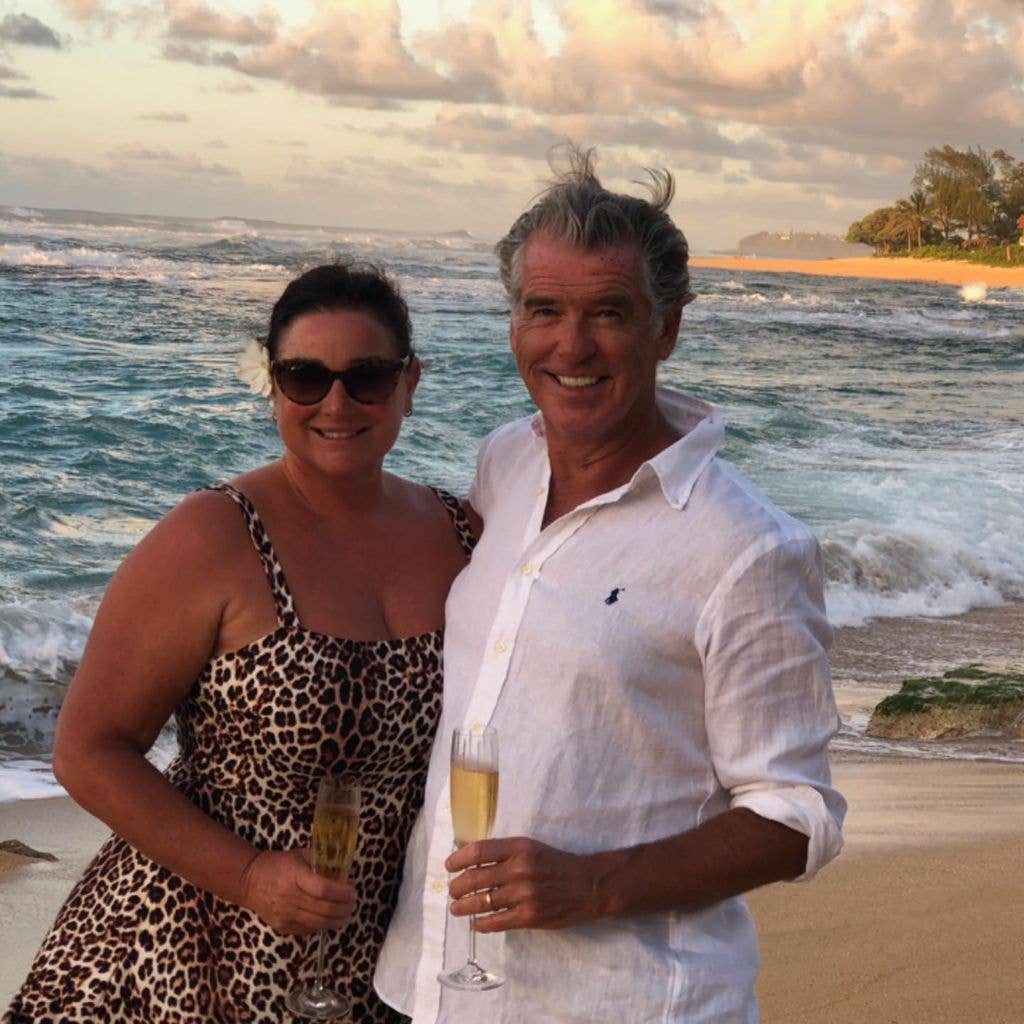 Pierce Brosnan and his wife Keely Shaye Brosnan pose for a photo on a beach holding champagne glasses, shared on Instagram