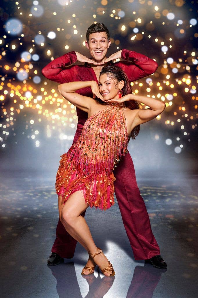 A man and a woman in red costumes dance together on a stage with sparkling lights.