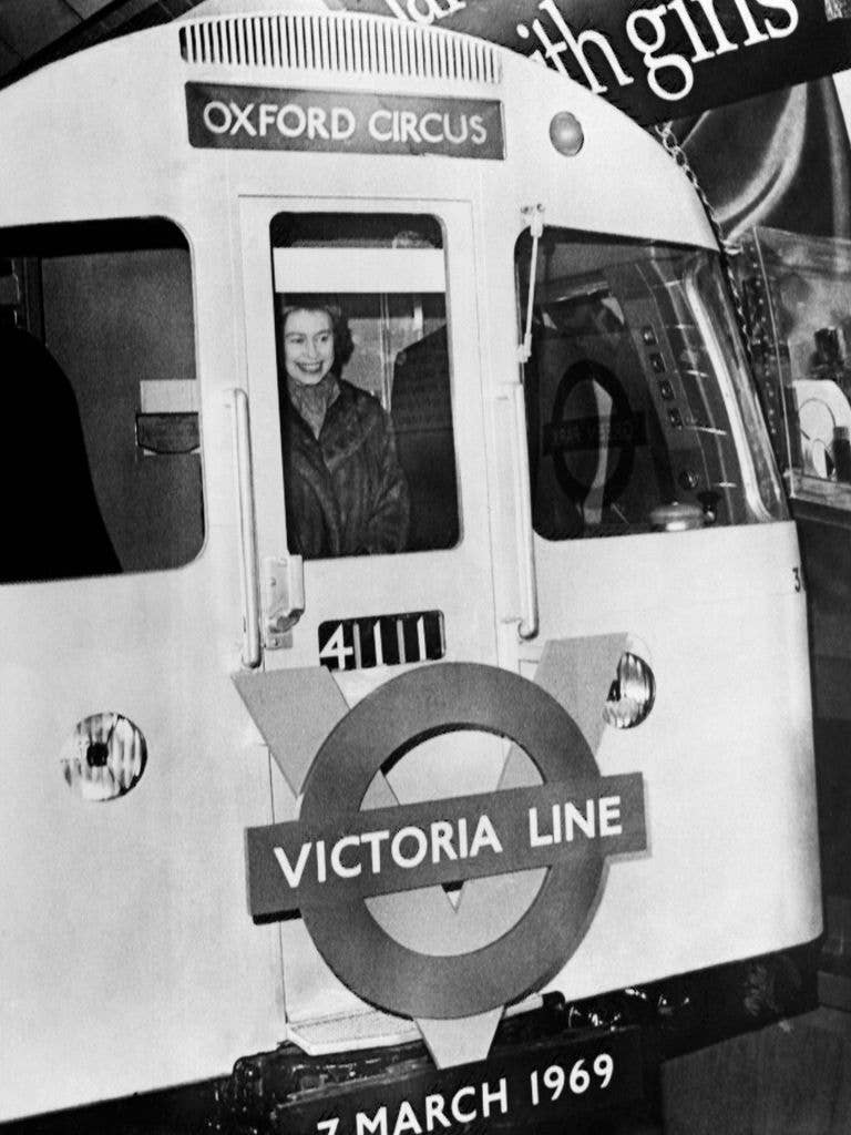 Black and white photo of Queen Elizabeth II smiling inside an Oxford Circus Victoria Line train.