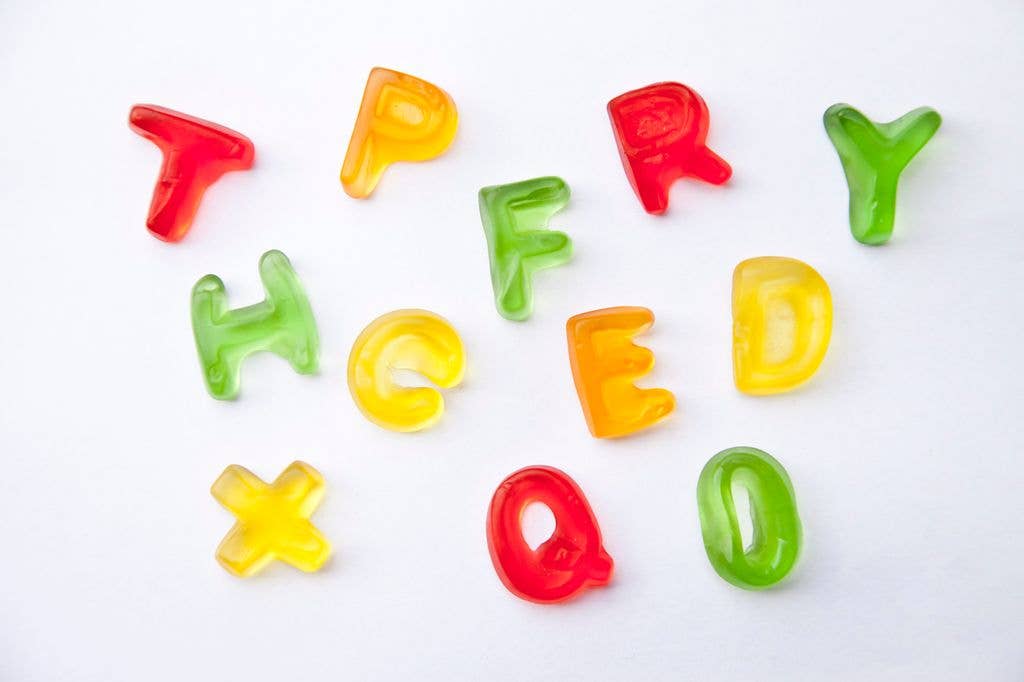 Brightly coloured jelly sweets shaped like capital letters, including T, P, R, Y, H, F, C, E, D, X, Q and O, are scattered on a white surface.