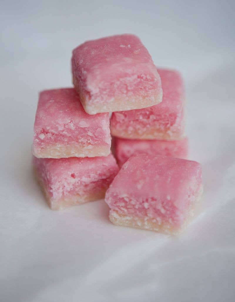 Several square pink candies with a sugary coating are stacked in a small pile against a soft white background.