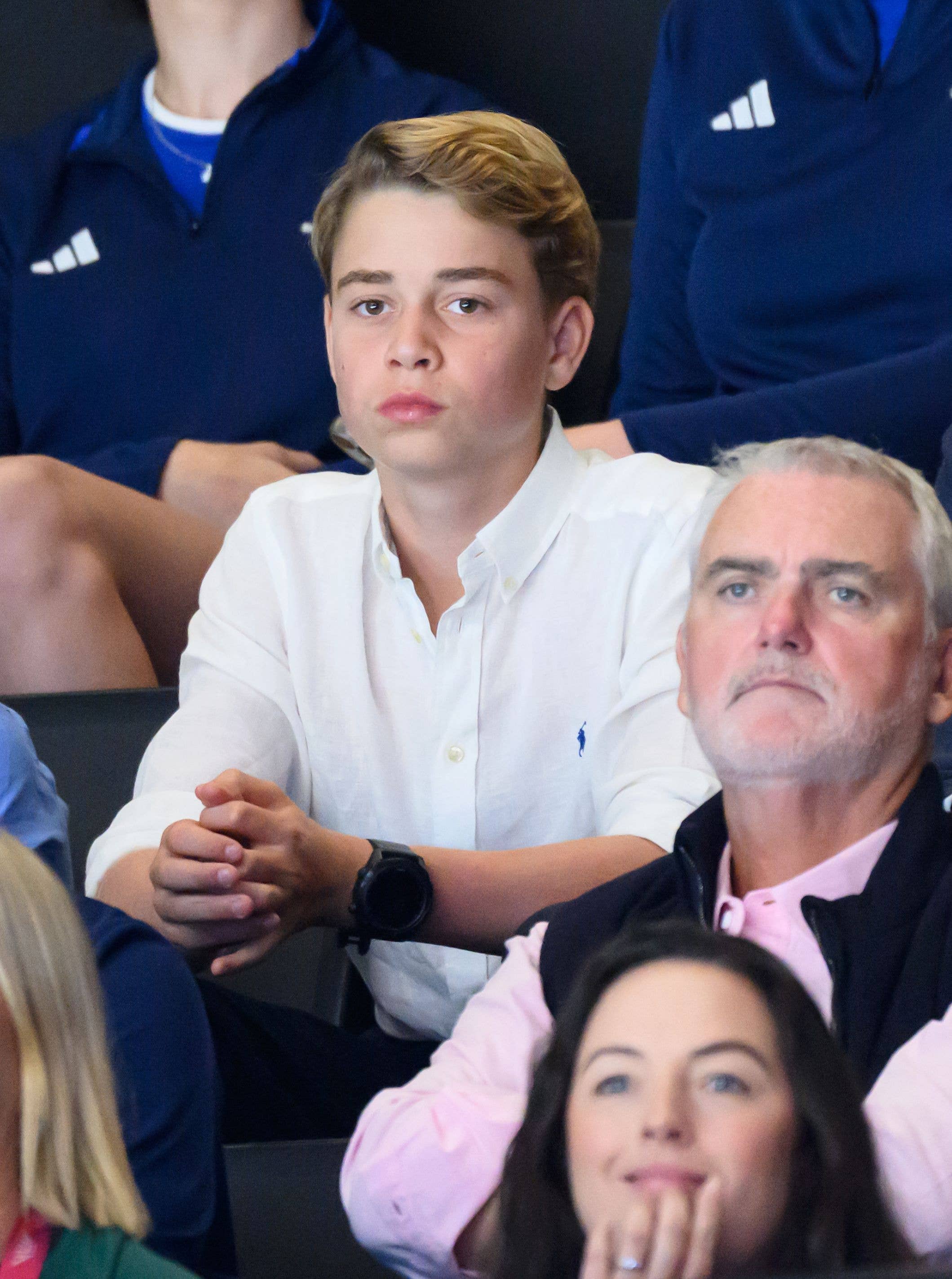 Prince George sits in stands with family, wearing white shirt