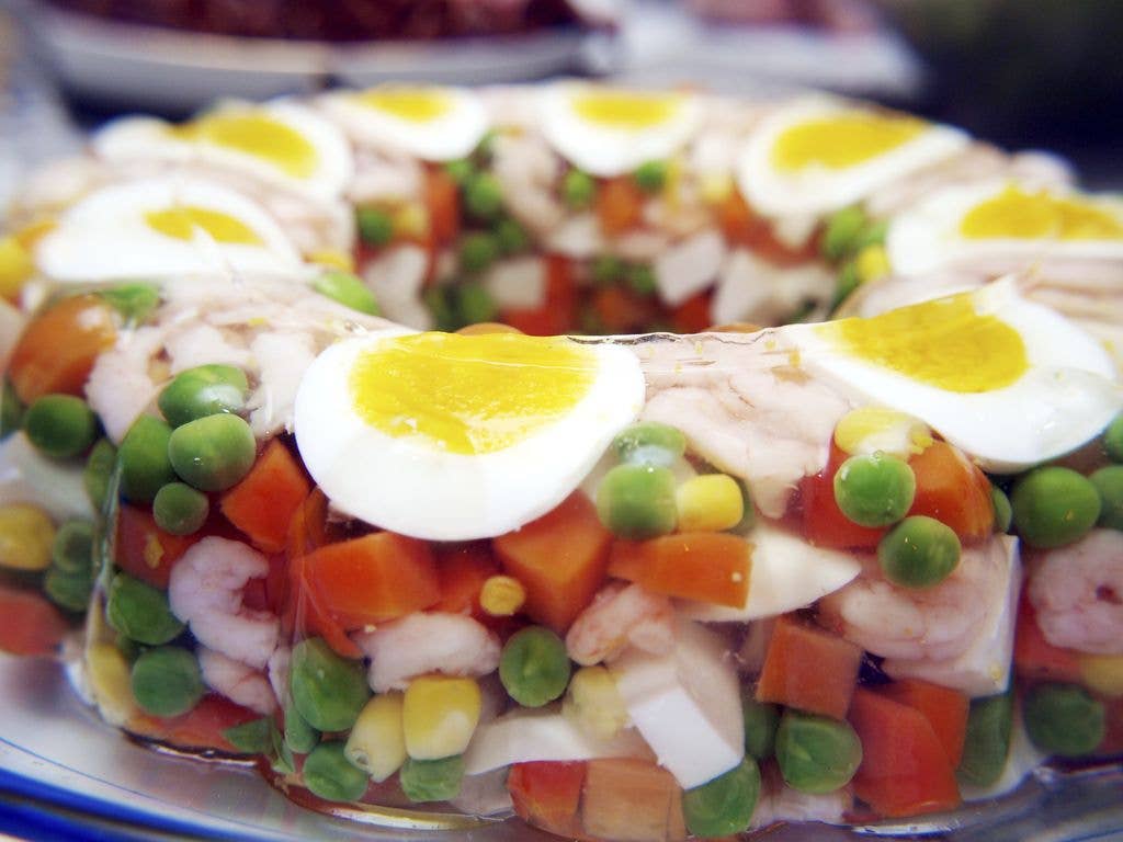 Close-up of a savoury jelly ring filled with prawns, diced carrot, peas and sweetcorn, garnished with slices of hard-boiled egg on top.
